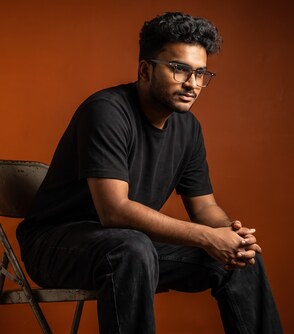 Yash Gandhi seated against an orange backdrop