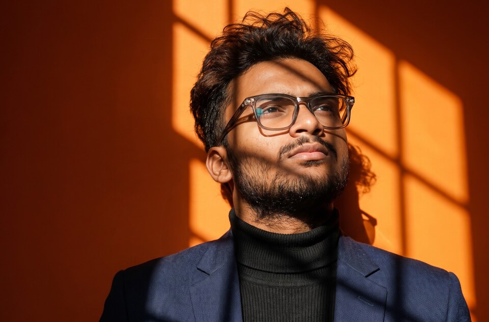 Yash Gandhi in glasses and a black turtleneck, lit by warm window light